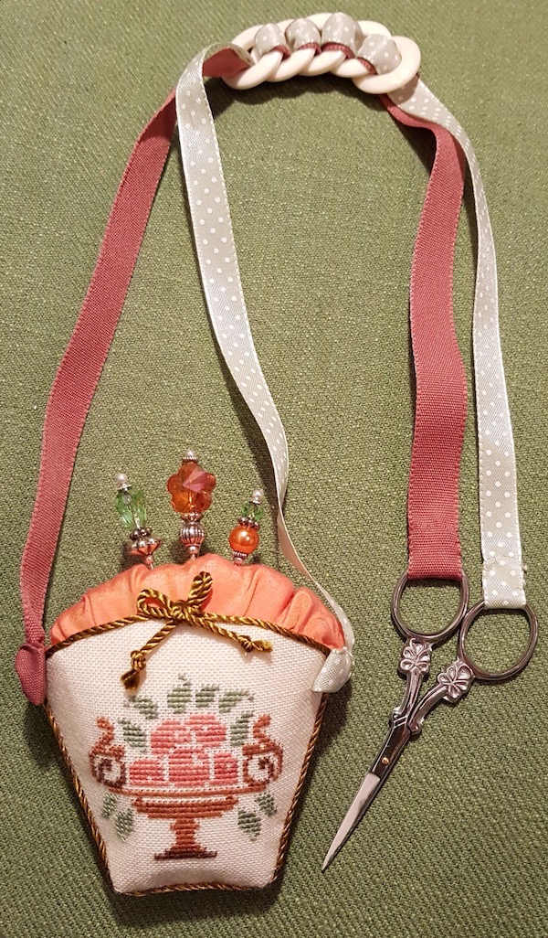 a sewing accessory with a basket pincushion and bone rings looped ribbon handles for scissors